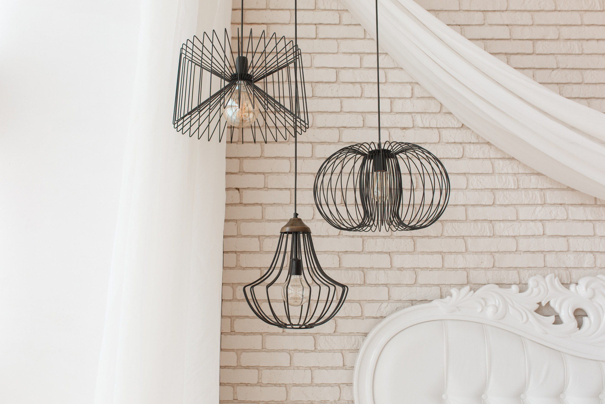 Three stylish light fixtures suspended from the ceiling illuminate a cozy bed, enhancing the room's ambiance.