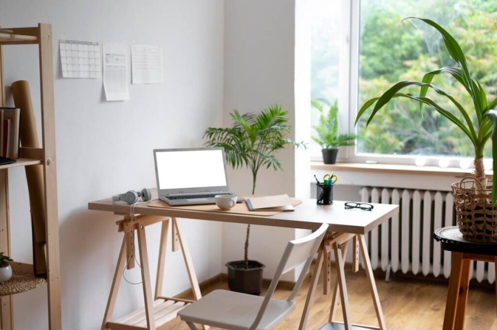 Bright and airy home office with a laptop, headphones, and plants near a window.