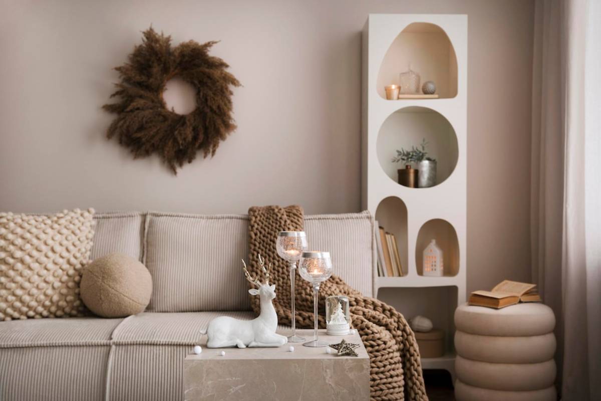 Cozy living room interior with beige sofa, decorative wreath, and built-in rounded shelves displaying plants and candles.