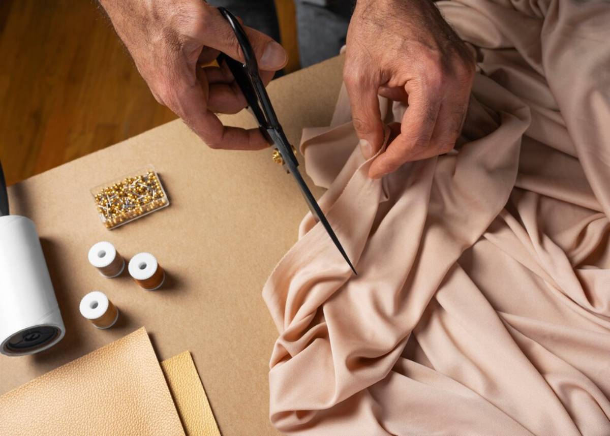 A person cutting fabric with scissors among sewing materials on a crafting table.