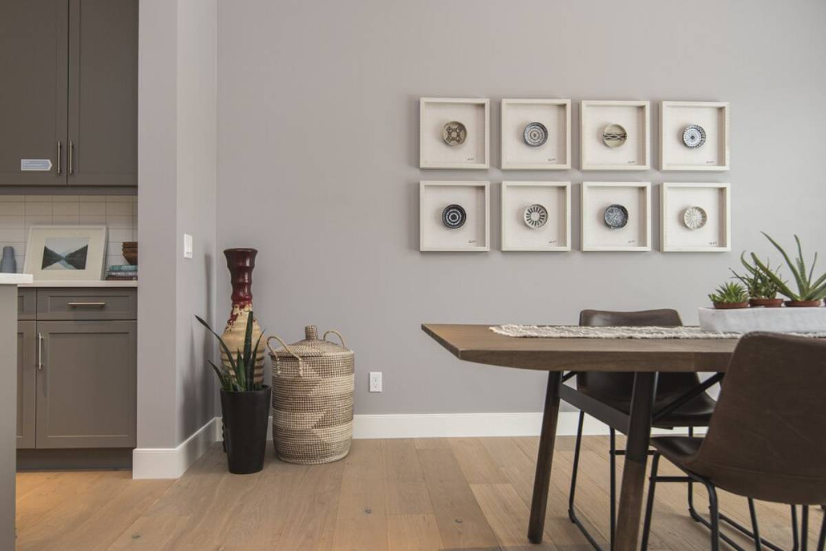 Modern dining area with a wooden table, artwork on the wall, and a kitchen visible in the background.