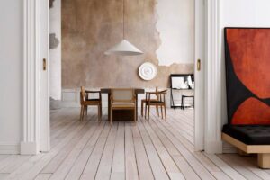 Minimalist dining area with wooden floors, distressed walls, modern furniture, and an abstract painting.