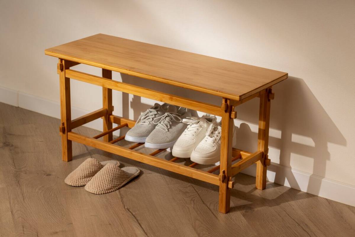 Wooden shoe rack with two shelves storing multiple pairs of shoes, topped with a flat surface, against a cream wall.