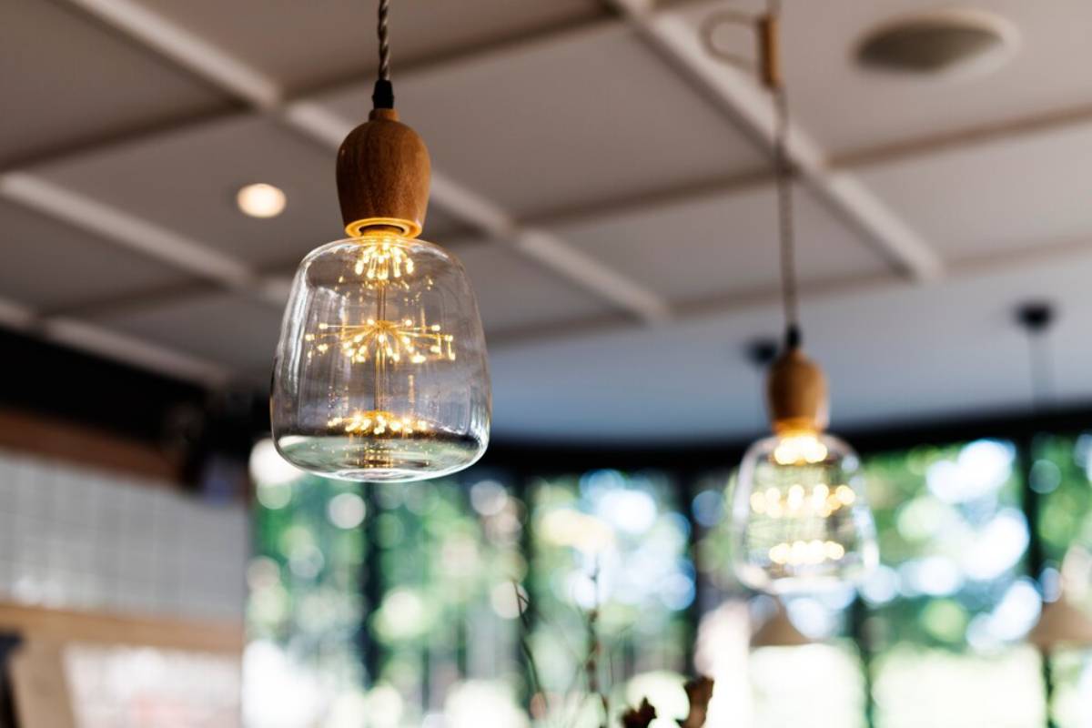 Modern glass pendant lights with glowing filaments hanging in a well-lit cafe interior.