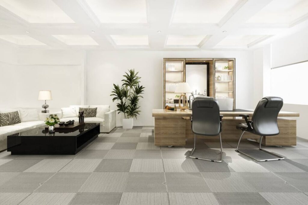 Modern office interior featuring a white sofa, black coffee table, desk with chairs, and a shelving unit in a bright room.