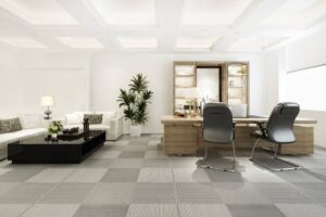 Modern office interior featuring a white sofa, black coffee table, desk with chairs, and a shelving unit in a bright room.
