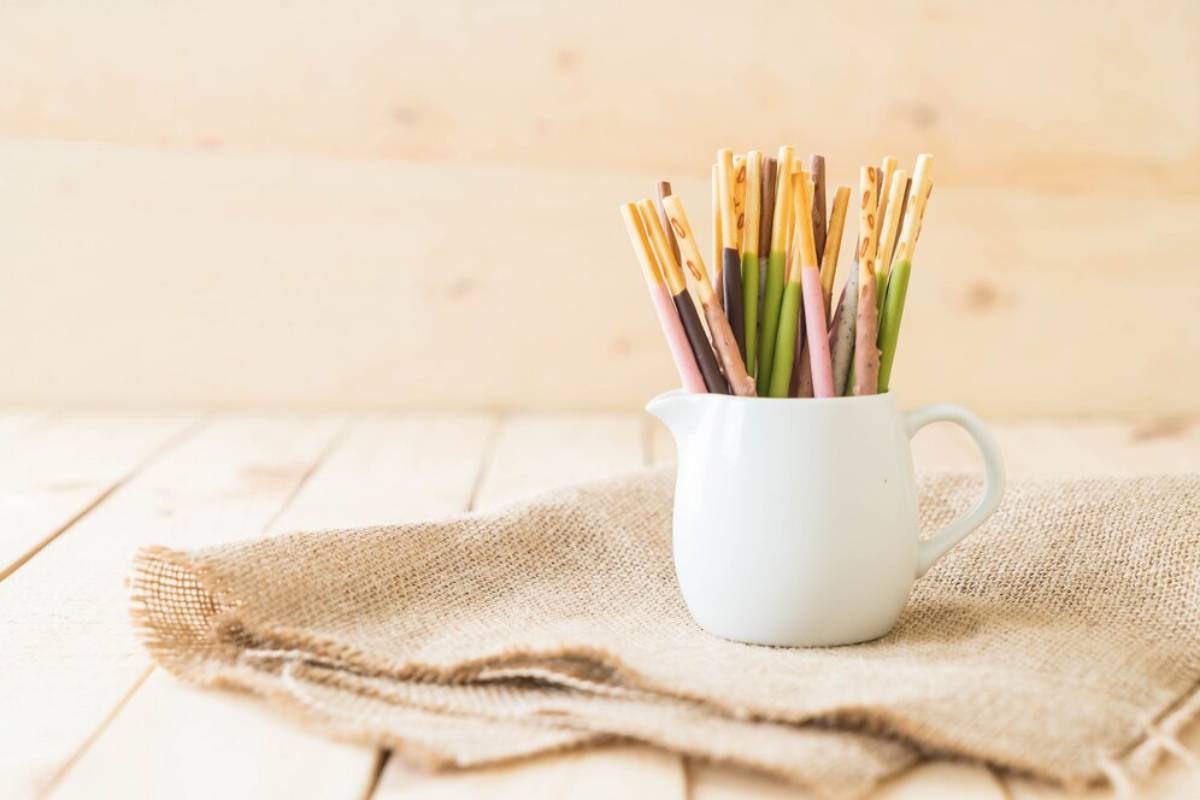 A white pitcher filled with colorful, decorative sticks sits atop a burlap cloth on a wooden table