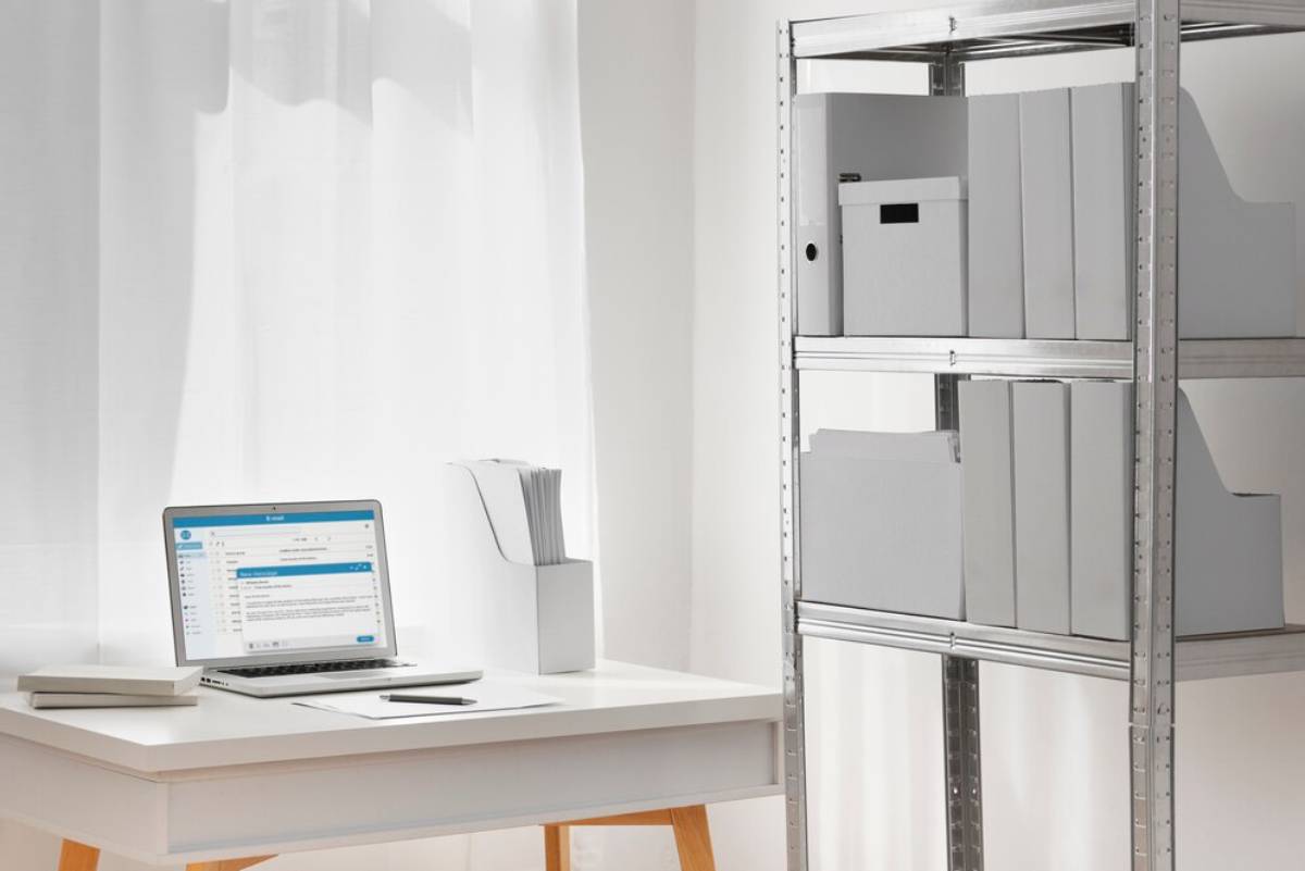 A modern workspace featuring a laptop on a white desk, organized paperwork