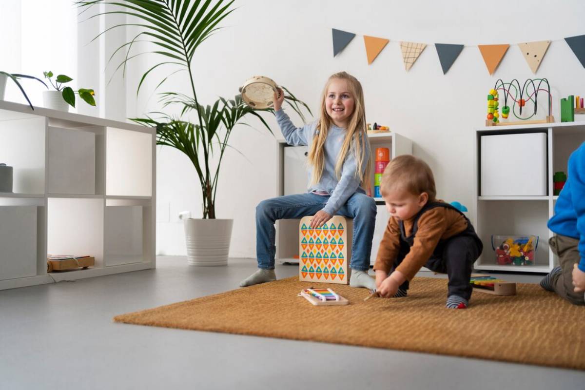 A young girl playing a tambourine while a toddler plays with toys in a bright playroom.