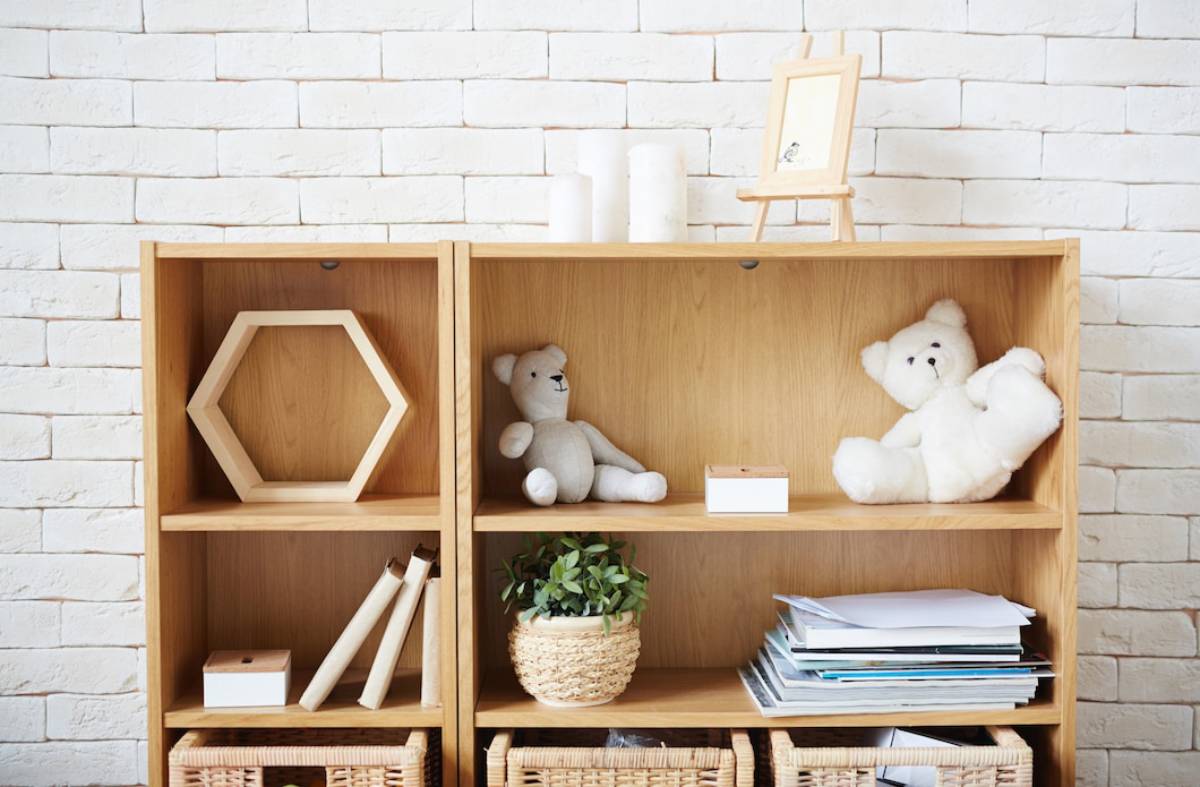 Wooden shelves with decorative items, plants, teddy bears, and books against a white brick wall.