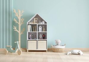 Child's playroom featuring a house-shaped bookshelf with toys, a wooden toy scooter, and a teddy bear in a basket.