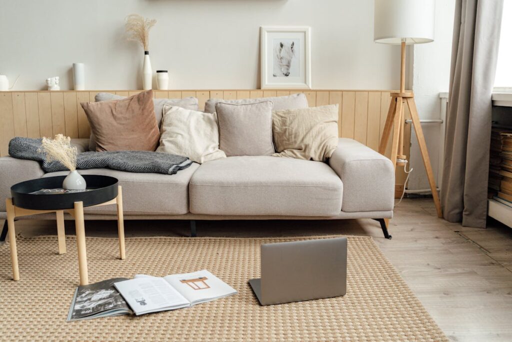 A cozy living room featuring a sectional sofa with pillows, a round coffee table, laptop, and a floor lamp.
