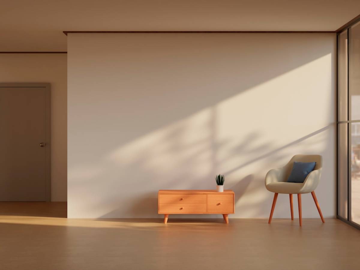 Minimalist room with a wooden dresser, modern armchair, and sunlight casting shadows on a plain wall.
