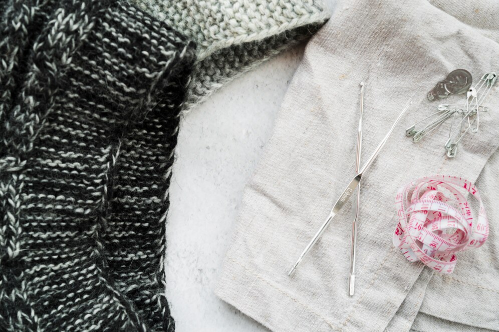 A pair of knitting needles crossed with a pair of scissors on a flat surface, showcasing crafting tools.